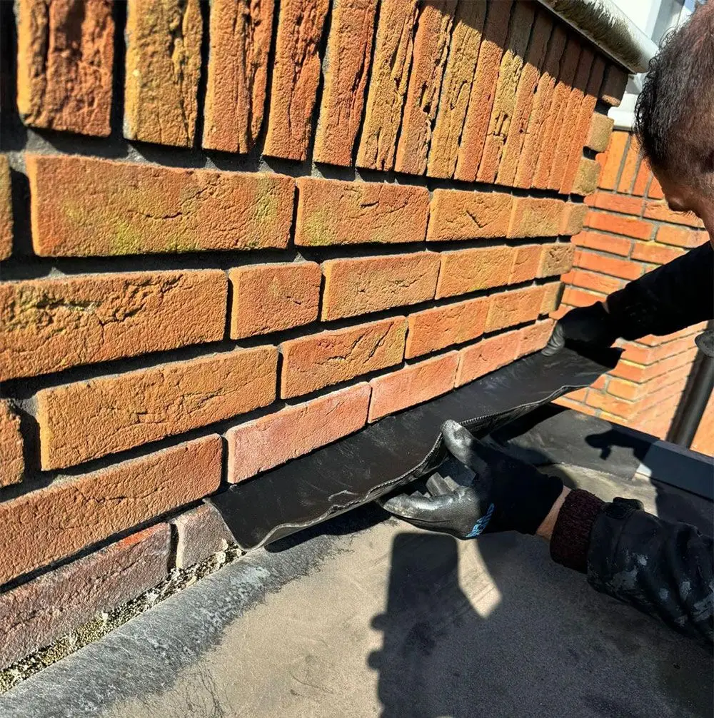Dakdekker werkt aan de aansluiting van de dakbedekking tegen een muur
