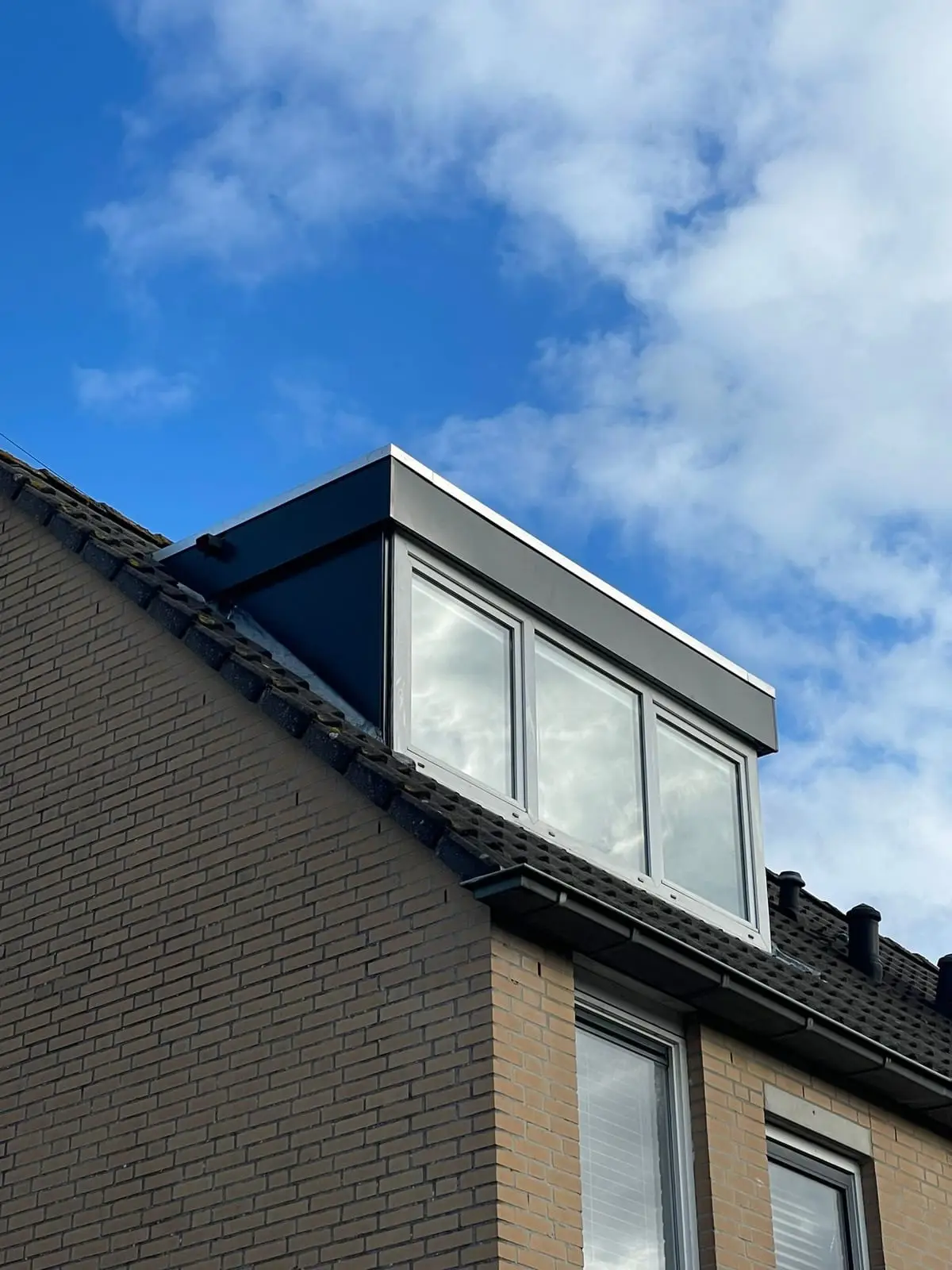 Dakkapel met drie ramen in een dak met zwarte pannen