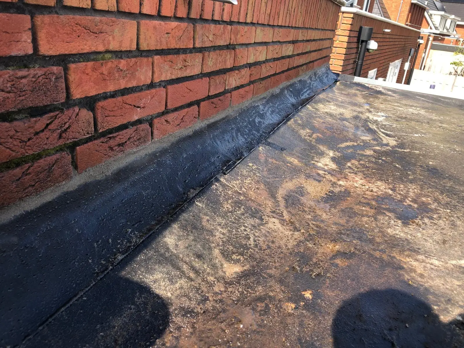 Nieuwe strook bitumen tegen een bakstenen muur, op een verweerd plat dak