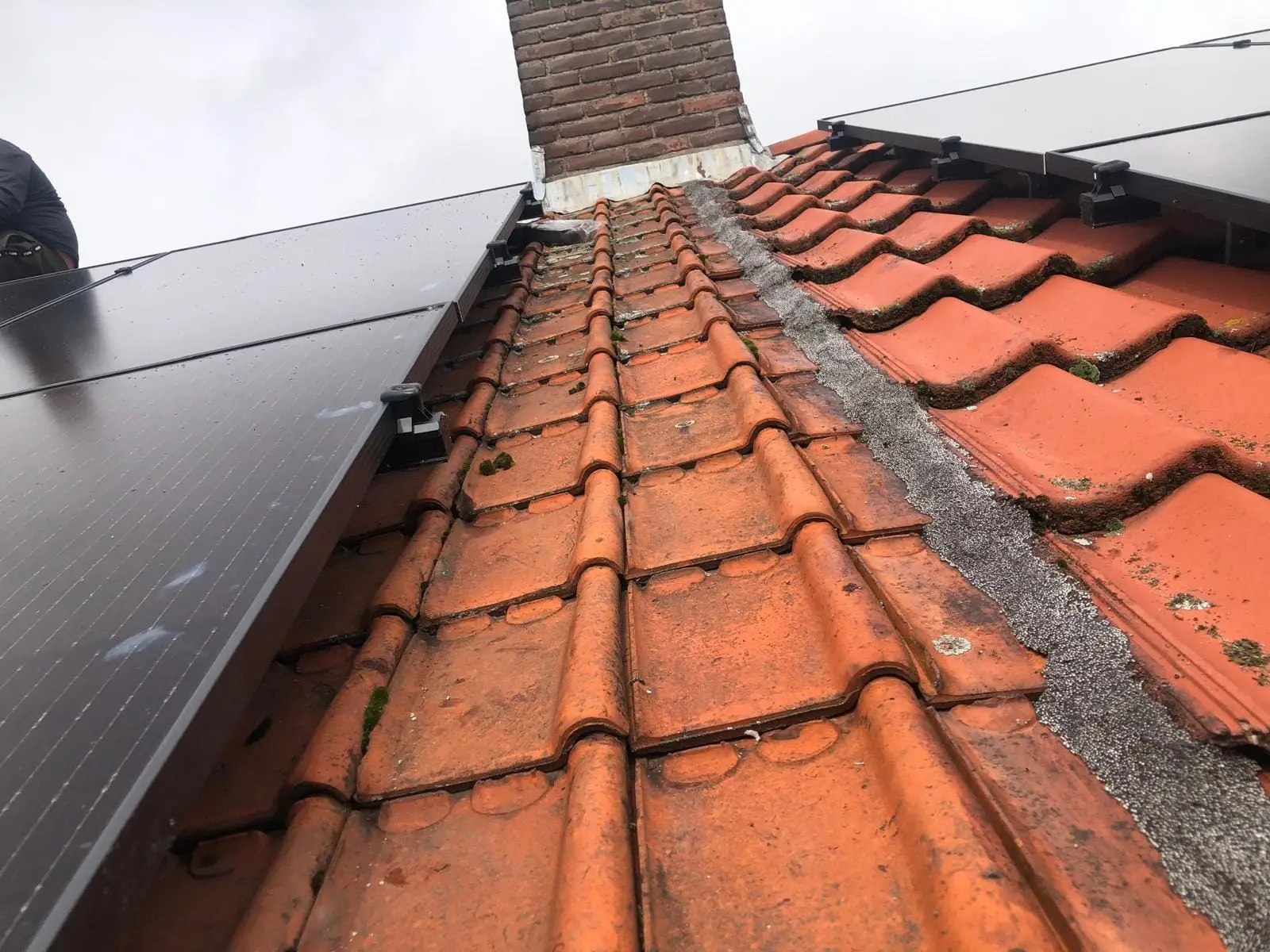 Oranje dakpannen tussen zonnepanelen en een gemetselde schoorsteen