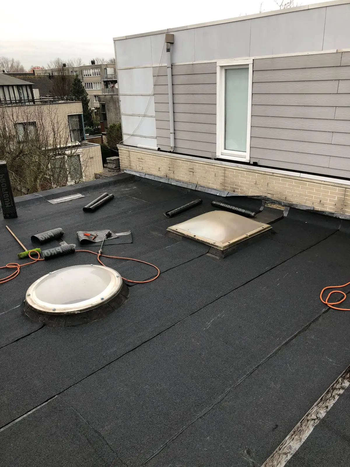 Nieuw plat dak met bitumen, een ronde en een vierkante lichtkoepel